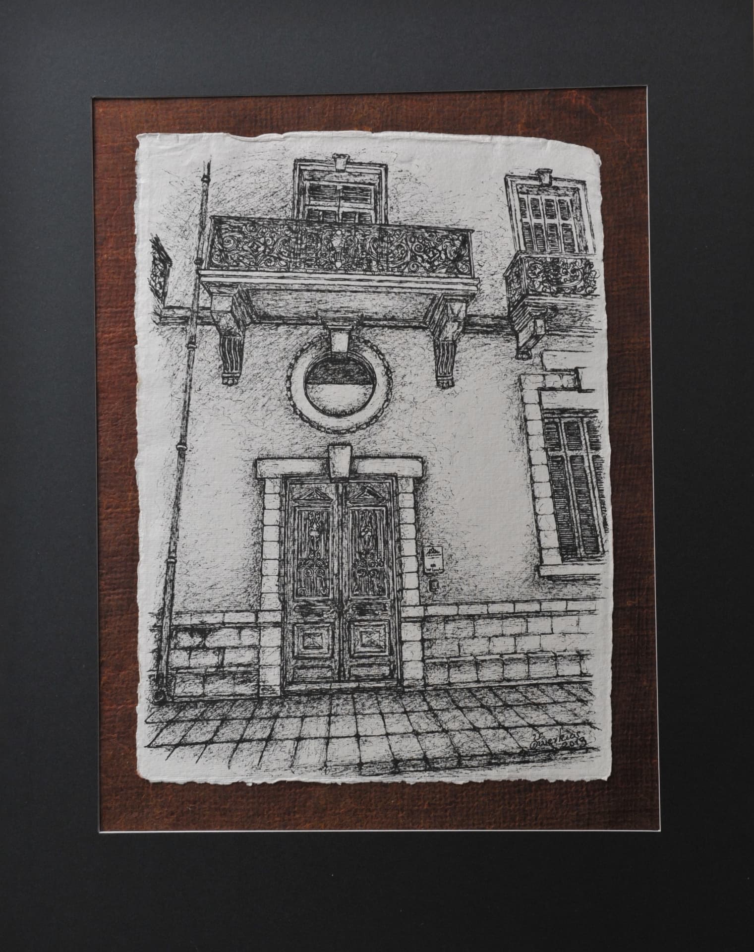 Ink drawing of a building facade with a paved street, double door, round window and wrought-iron balconies, on paper mounted on a reddish-brown mat