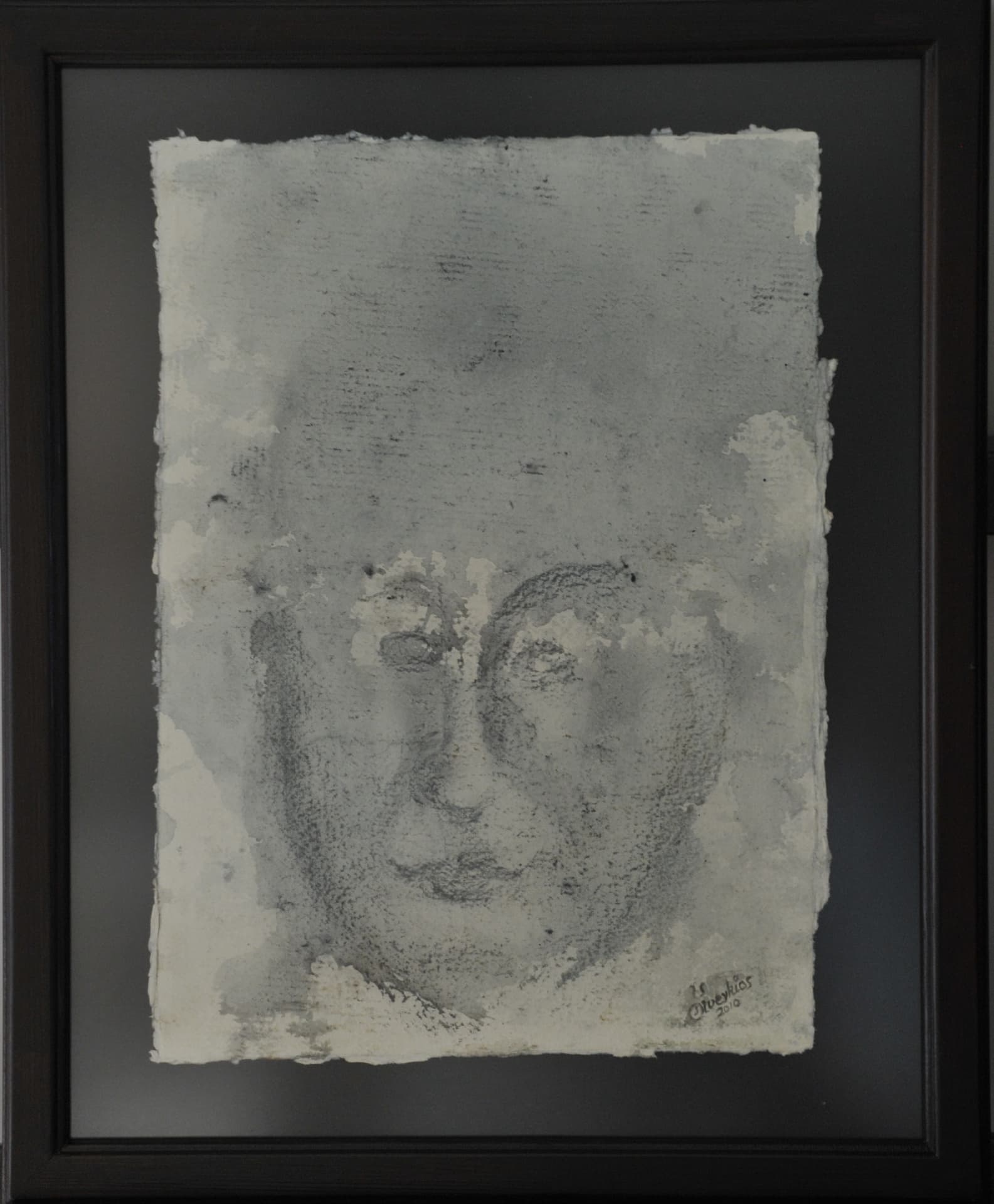 Frontal face in grained grey drawing marks and fluid washes on deckle-edged paper mounted on a dark mat