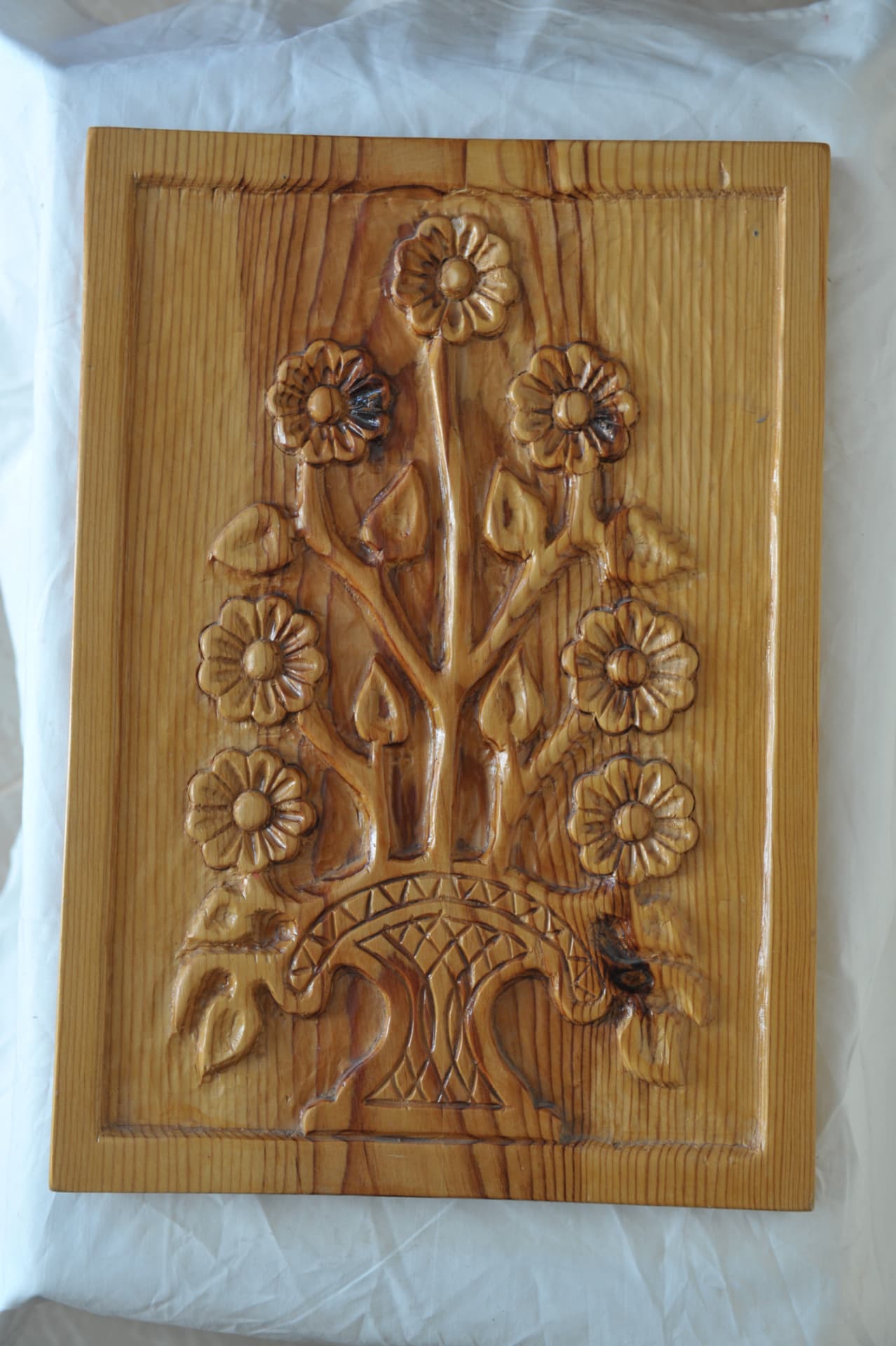 Rectangular wood relief of flowers and stems rising from a decorated vase