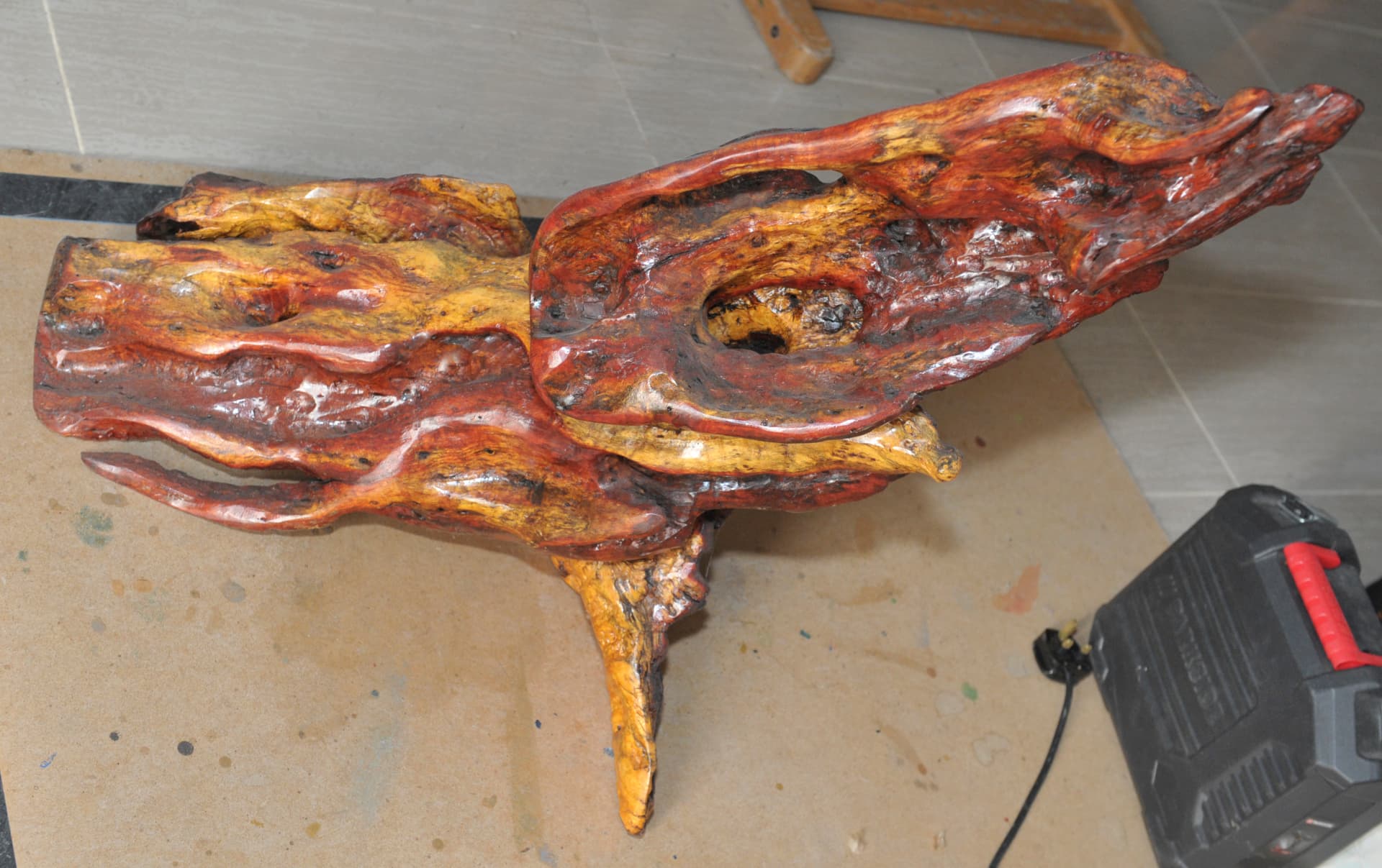 Polished branching wood form with reddish and golden surfaces on a workbench