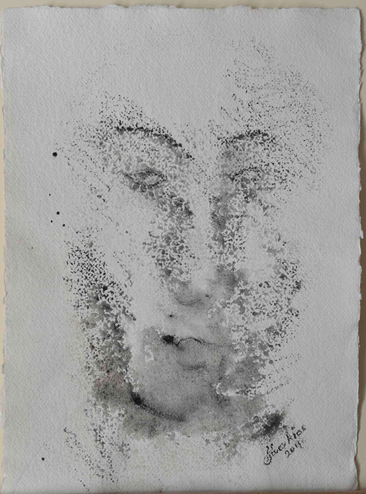 Faint face emerging from grey speckled and splattered ink on white deckle-edged paper