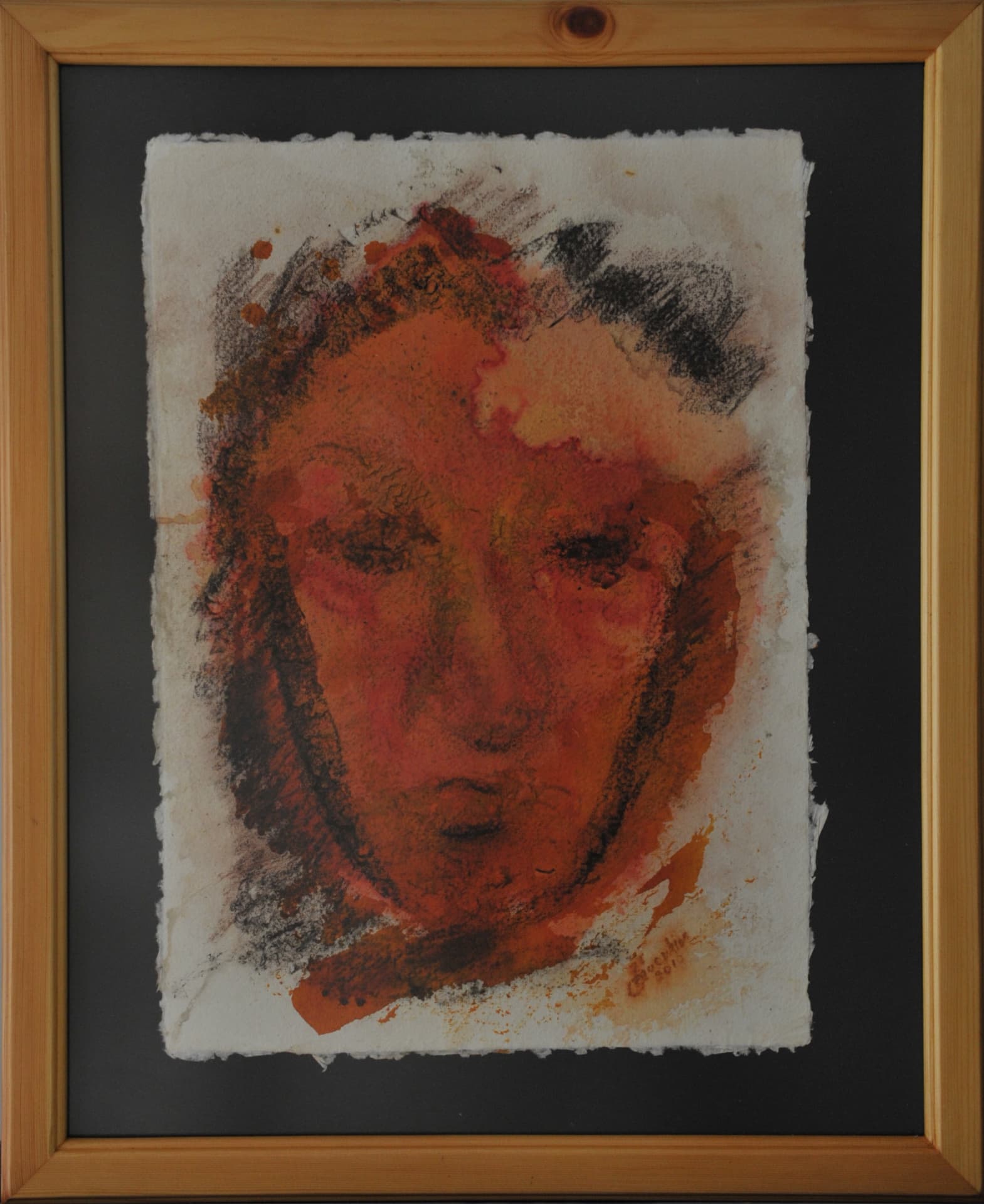 Close-up frontal face with dark eye sockets and prominent cheek contours, in terracotta and charcoal on deckle-edged paper mounted on a black mat
