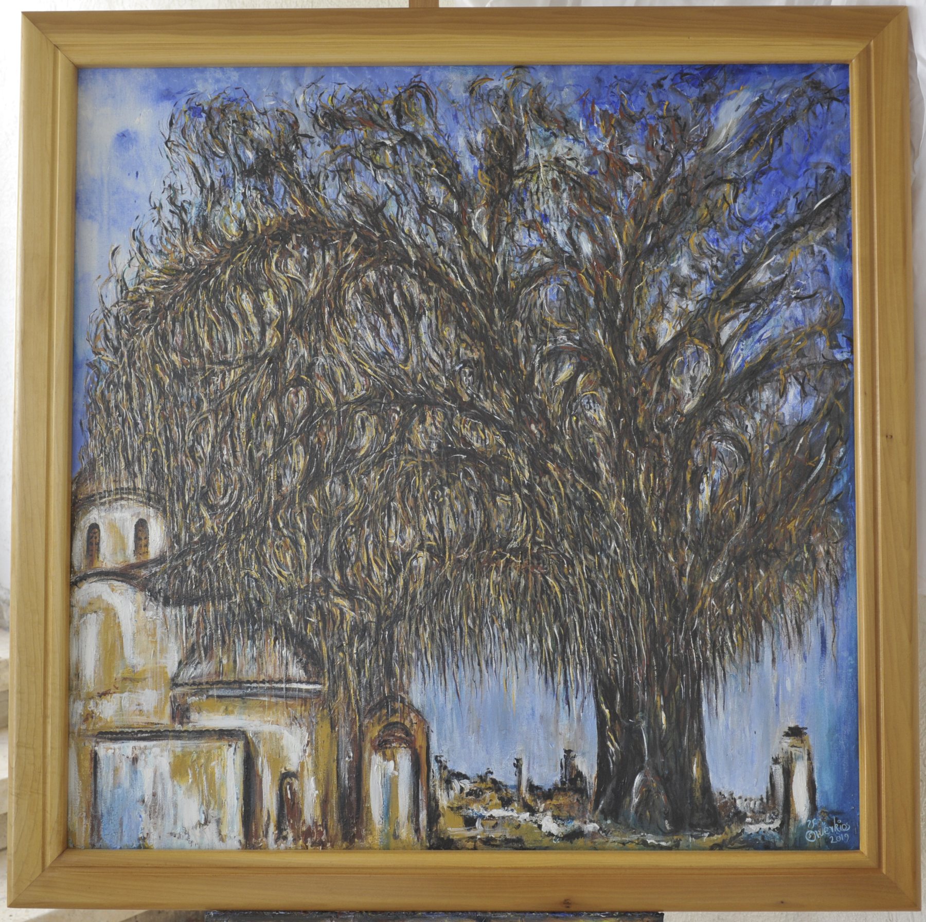 Painting of a large tree beside a pale building against a blue sky, in a wooden frame