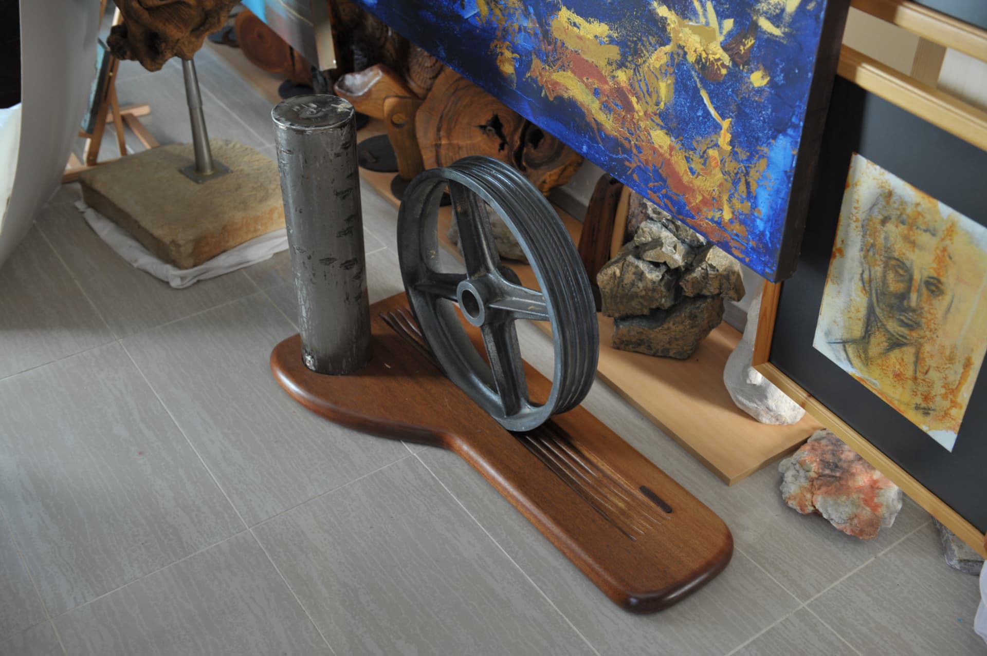 Long wood base carrying an upright metal cylinder and a grooved wheel, with parallel grooves carved along its top surface