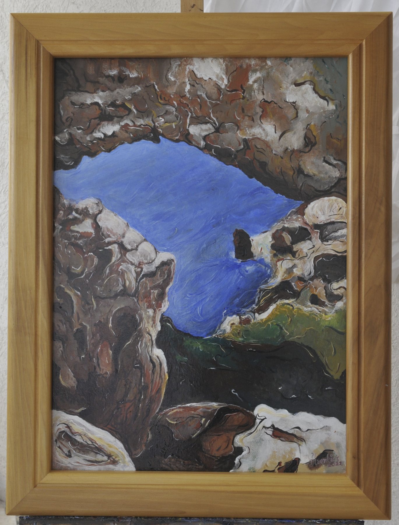 Painting of rocky formations encircling an opening of blue, in brown, grey and dark green, in a wooden frame