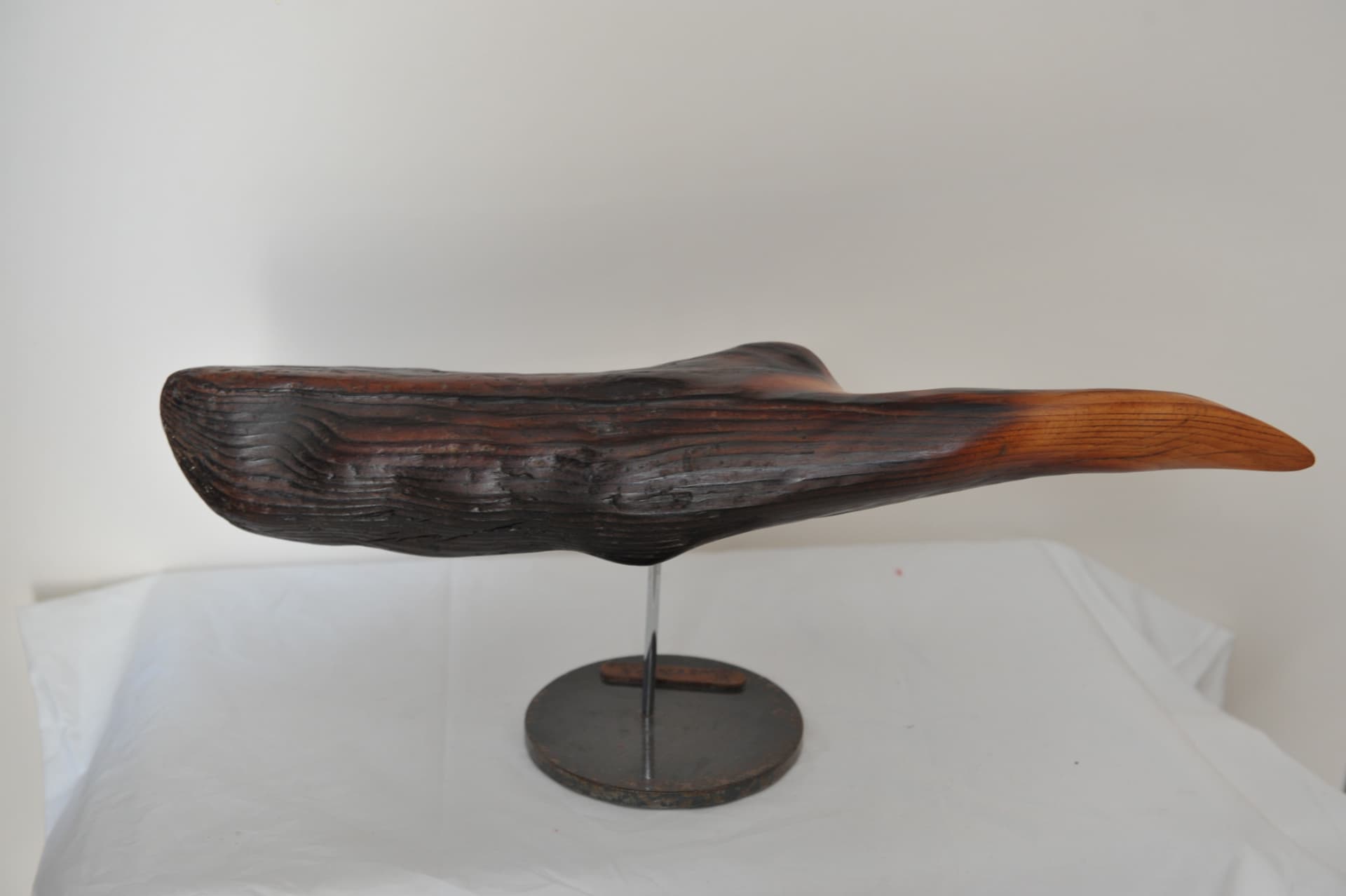 Horizontal wood form on a slender chrome rod, dark and grooved at one end, tapering to a smooth honey-coloured tip