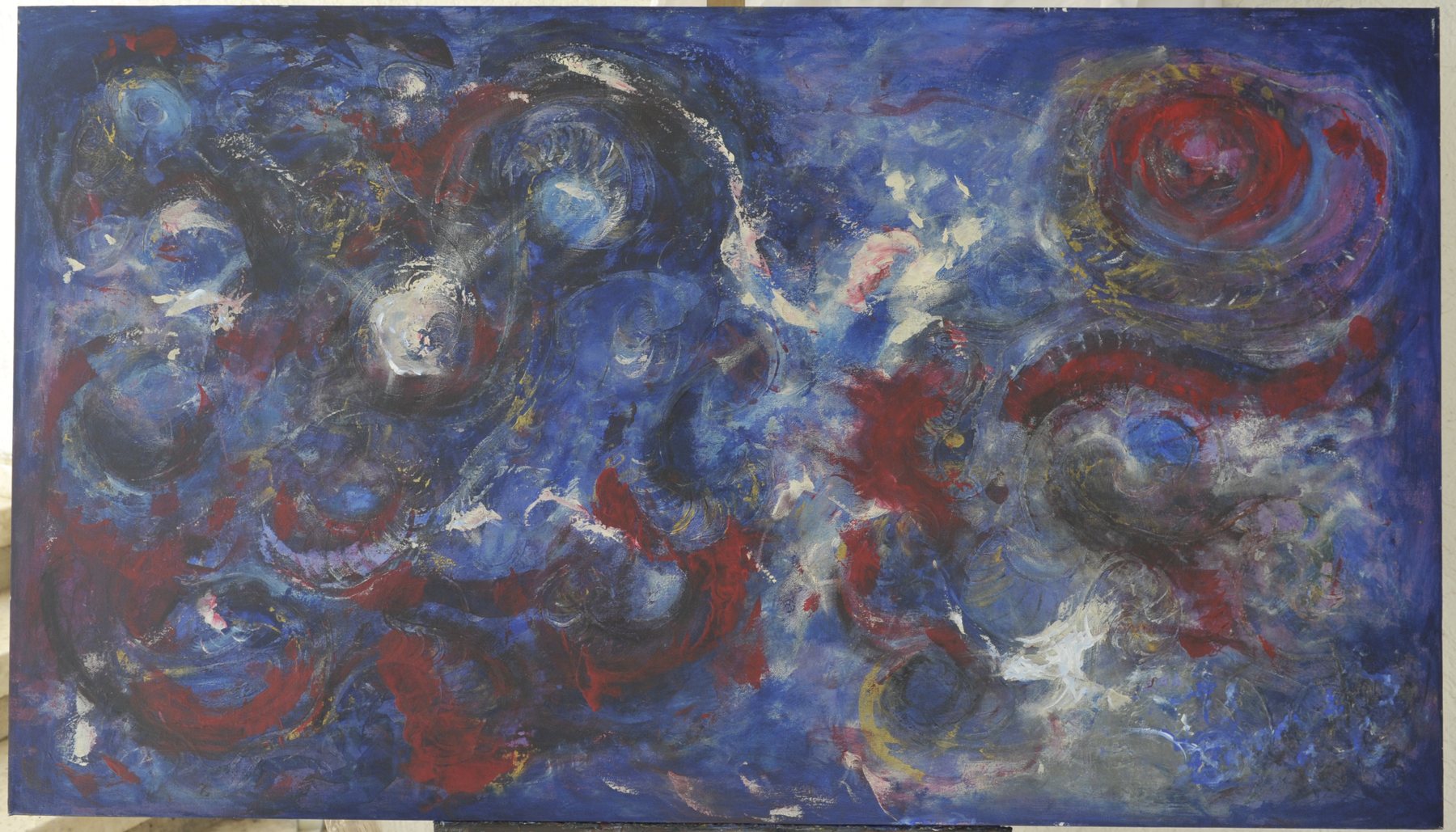 Landscape-format abstract painting with swirling circular patterns and mottled textures in deep blue and dark red