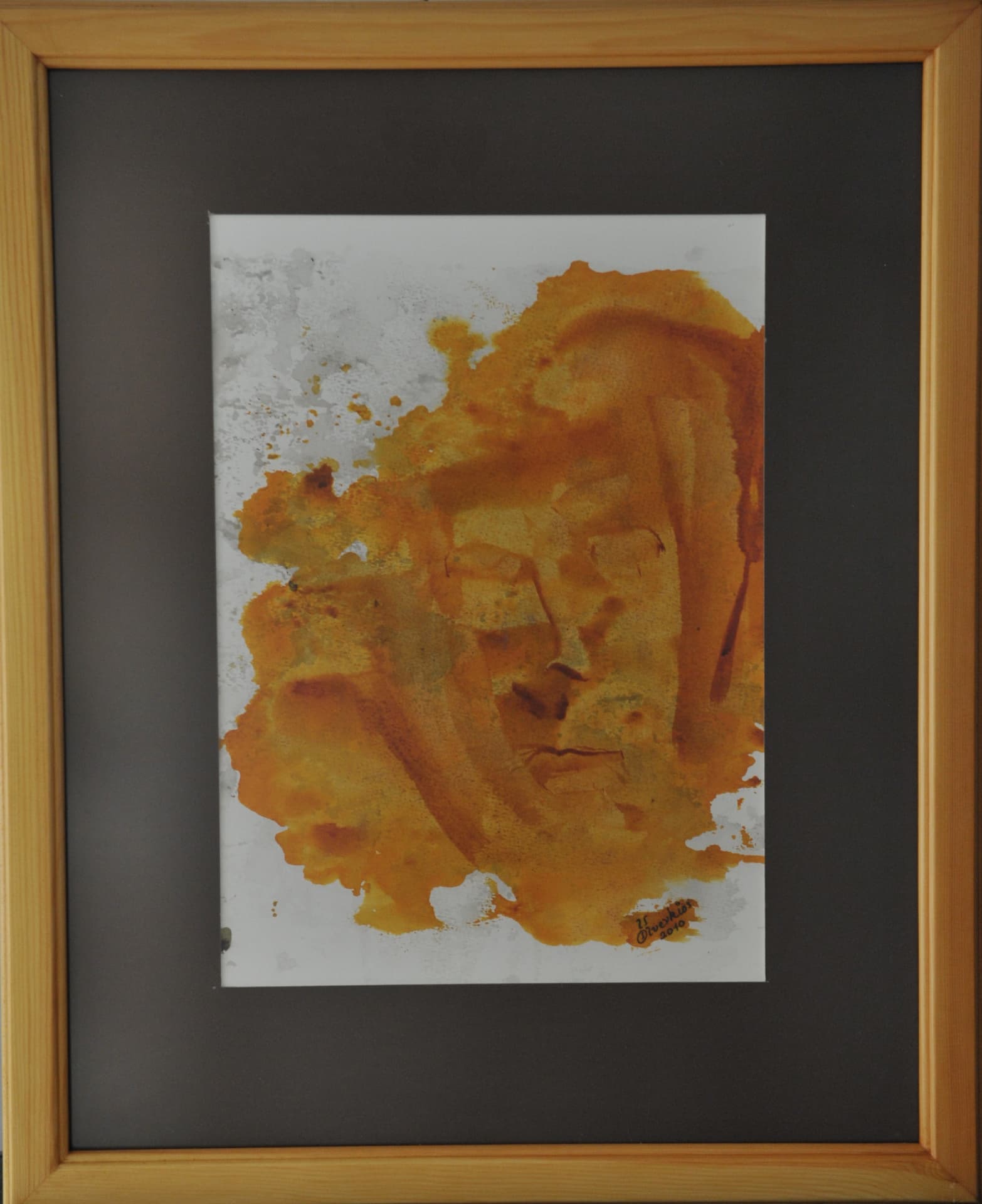 Face emerging faintly from an amber wash stain with grey splatters around it, on paper mounted on a dark mat in a light wood frame