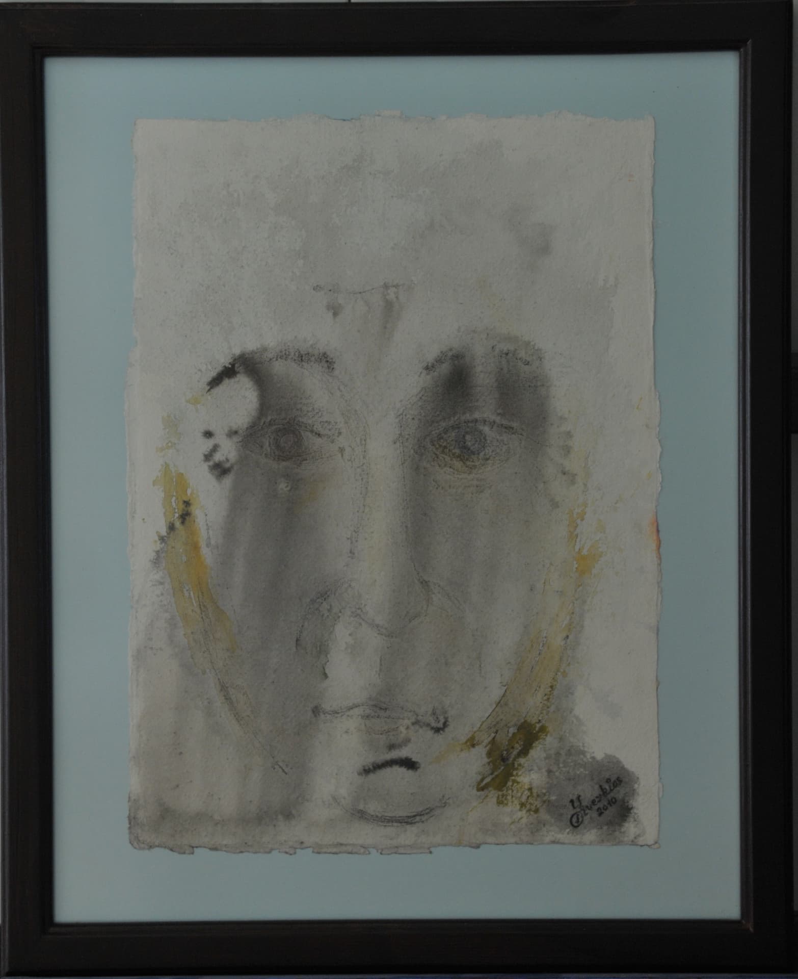 Faint frontal face rendered in soft charcoal grey with pale yellow accents on deckle-edged paper, mounted on a pale blue-grey mat