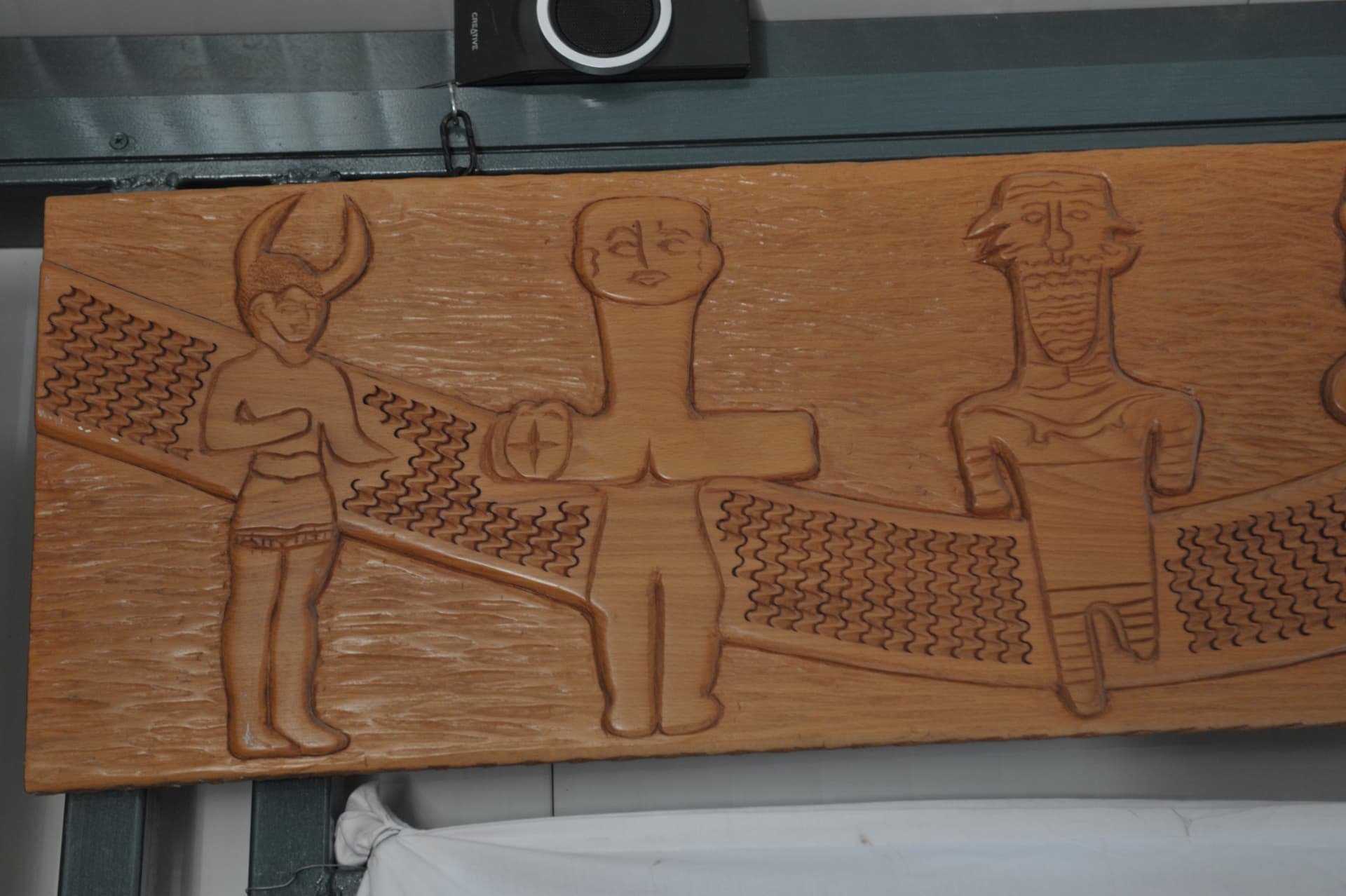 Horizontal wood relief panel carved with three stylized figures, the central one with outstretched arms and a disc
