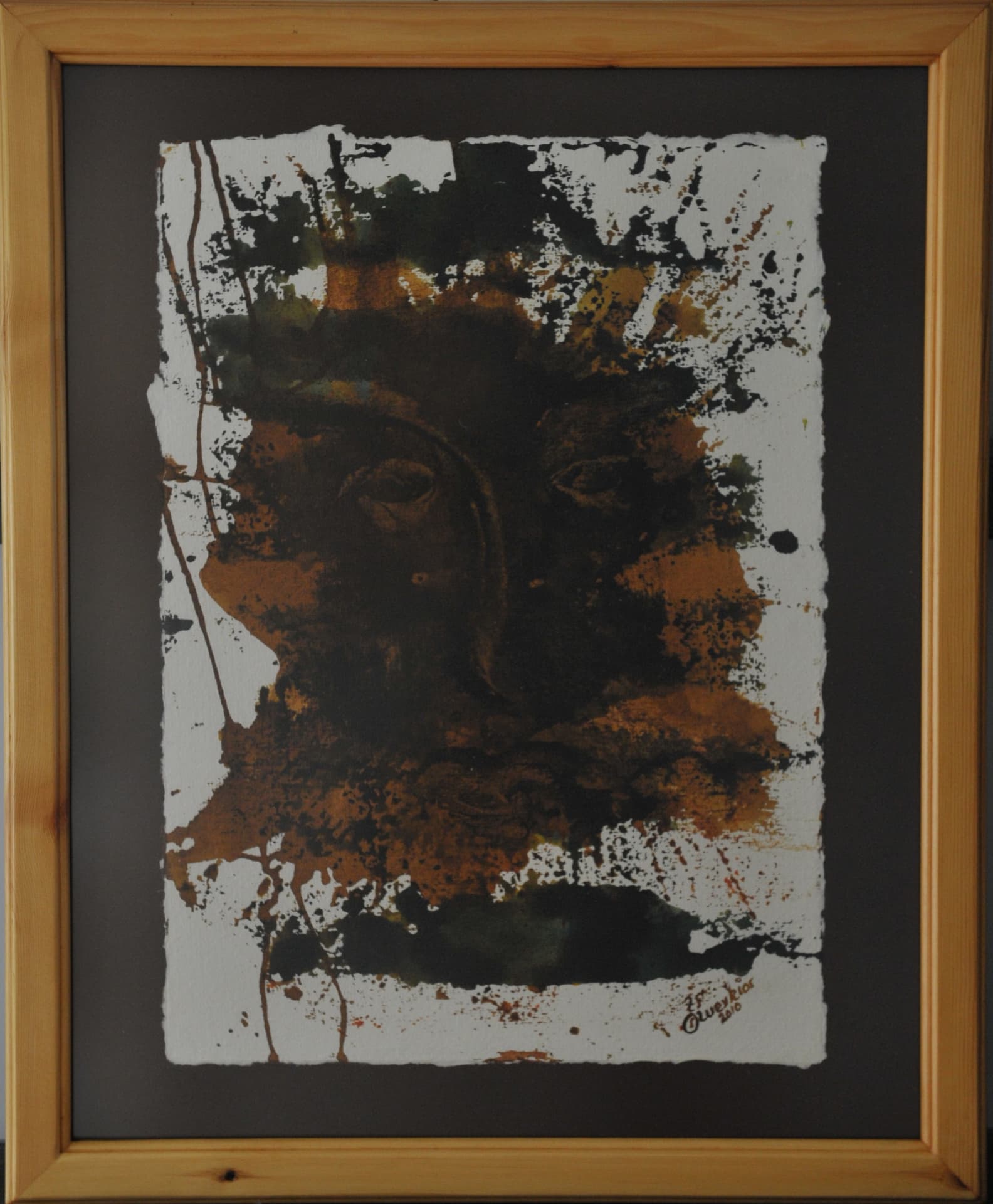 Face set within pooled ochre and dark green-black ink splatters on deckle-edged paper mounted on a dark mat in a light wood frame