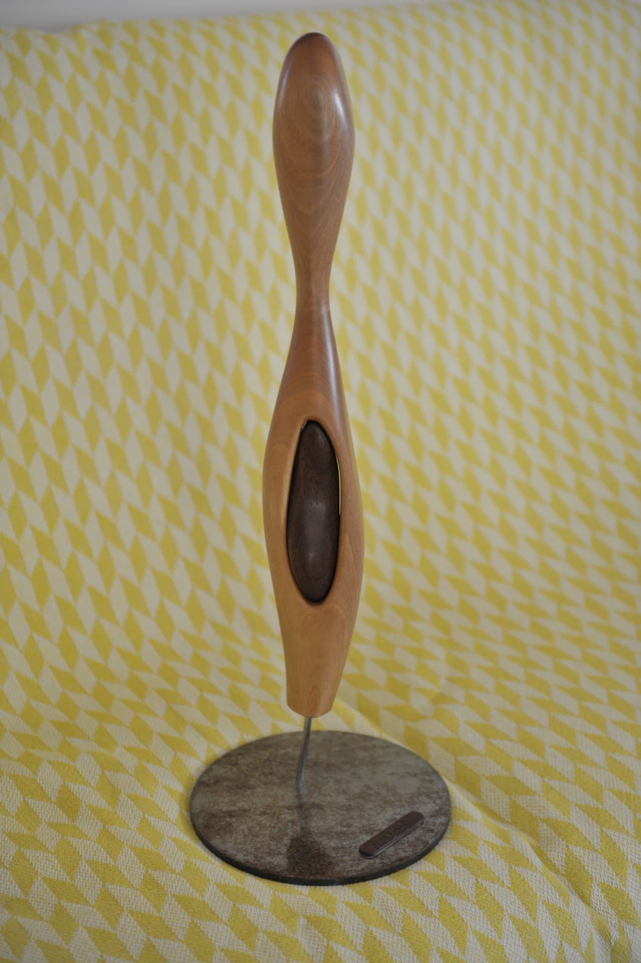 Slender polished wood sculpture with an oval opening on a circular stand