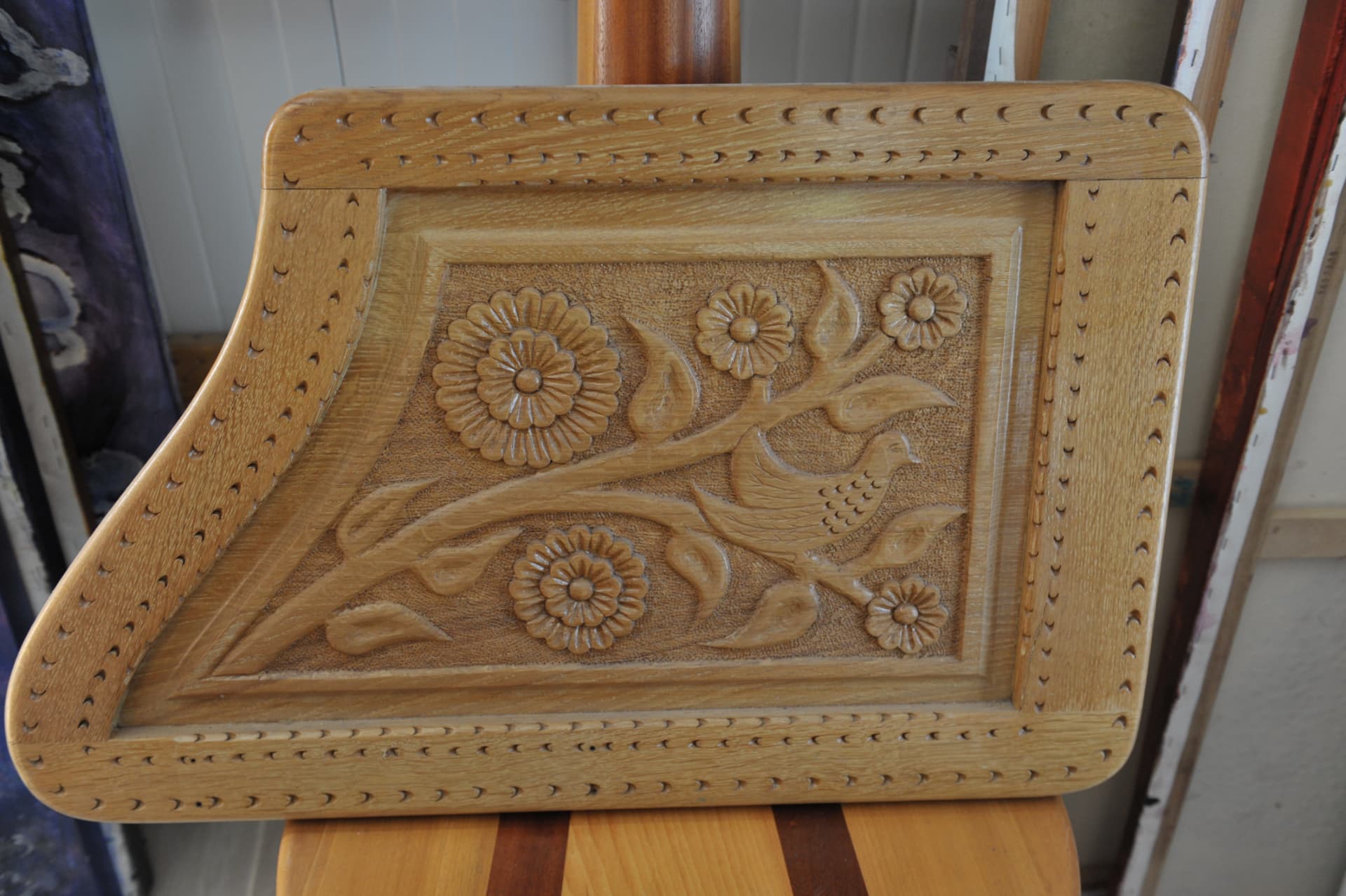 Wood relief panel carved with a flowering branch and a small bird, bordered by rows of crescent gouge marks, standing on a two-tone wooden surface