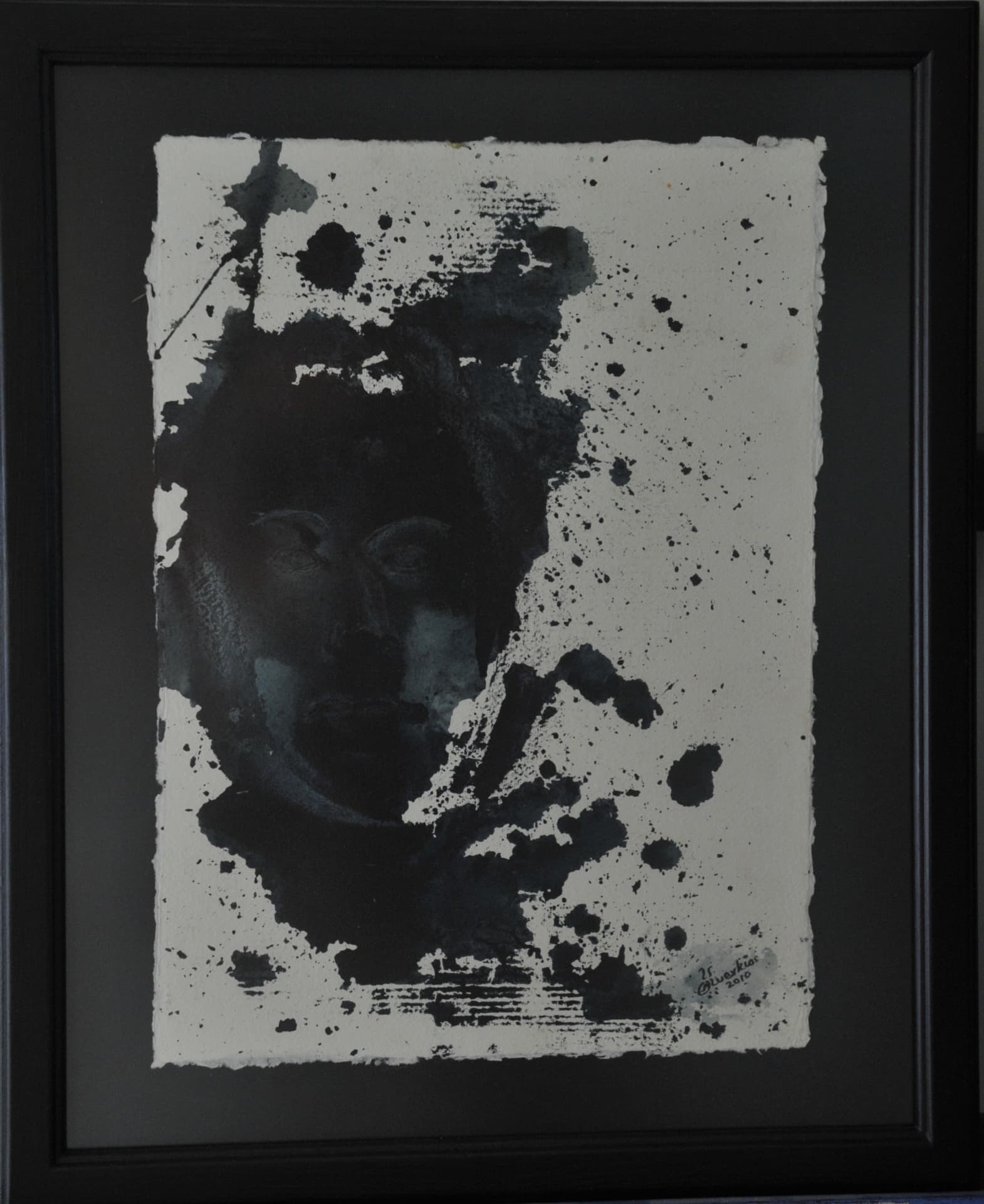 Face inside a splashed black ink silhouette with drips and specks on cream paper, on deckle-edged paper mounted on a charcoal mat
