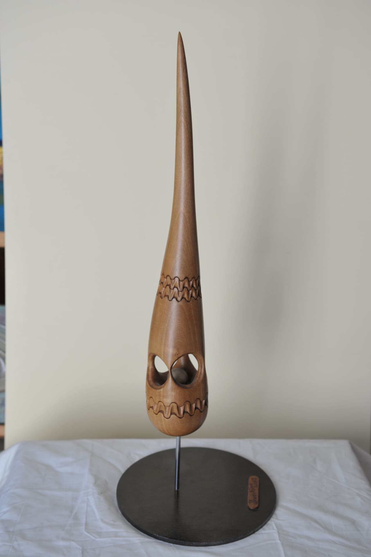 Tall tapering wood sculpture on a circular metal base, with two hollowed openings holding a loose carved sphere and carved zigzag bands