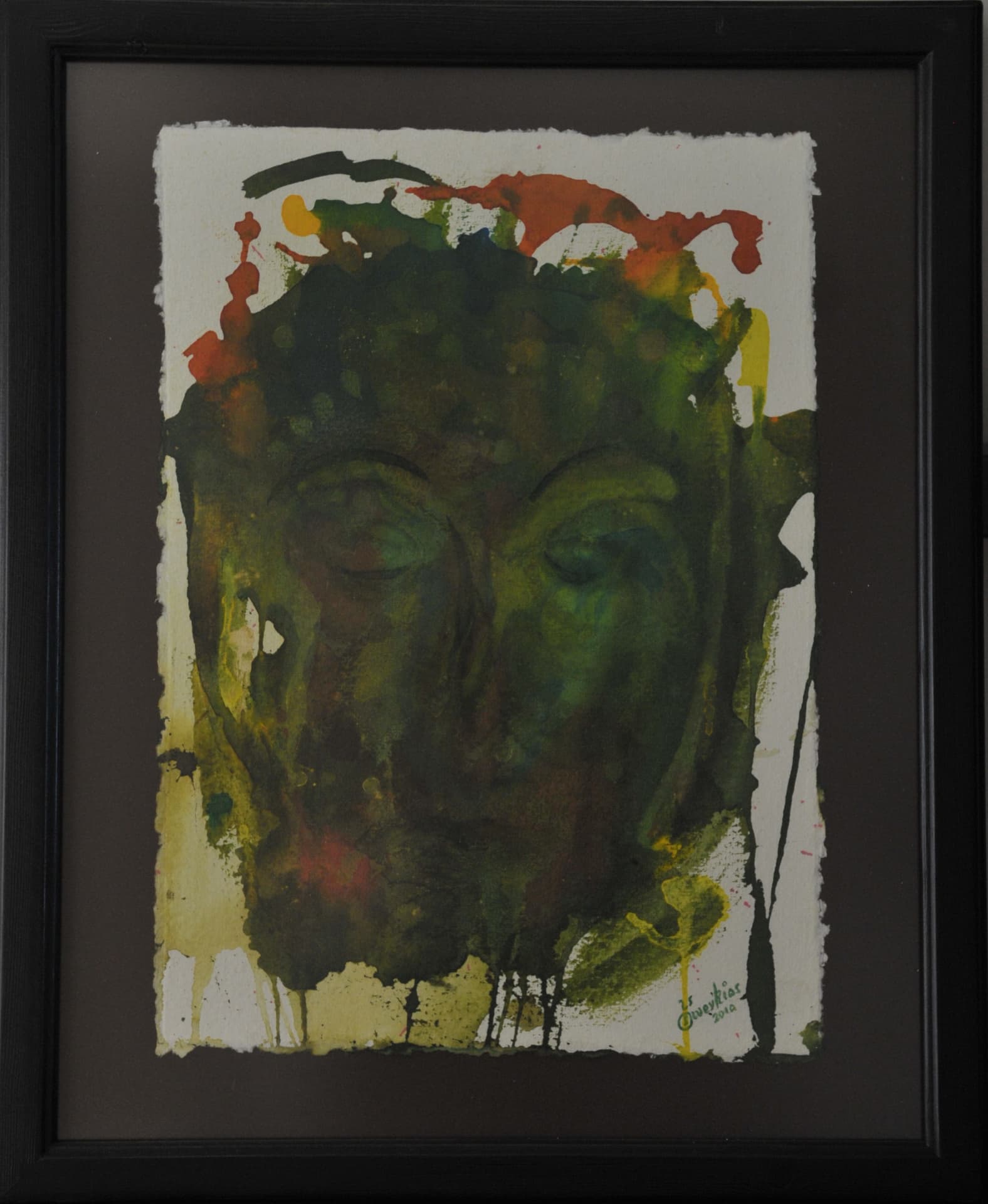 Face with closed eyes in dark green wash with vertical drips and splashes of orange, red and yellow, on deckle-edged paper mounted on a charcoal mat