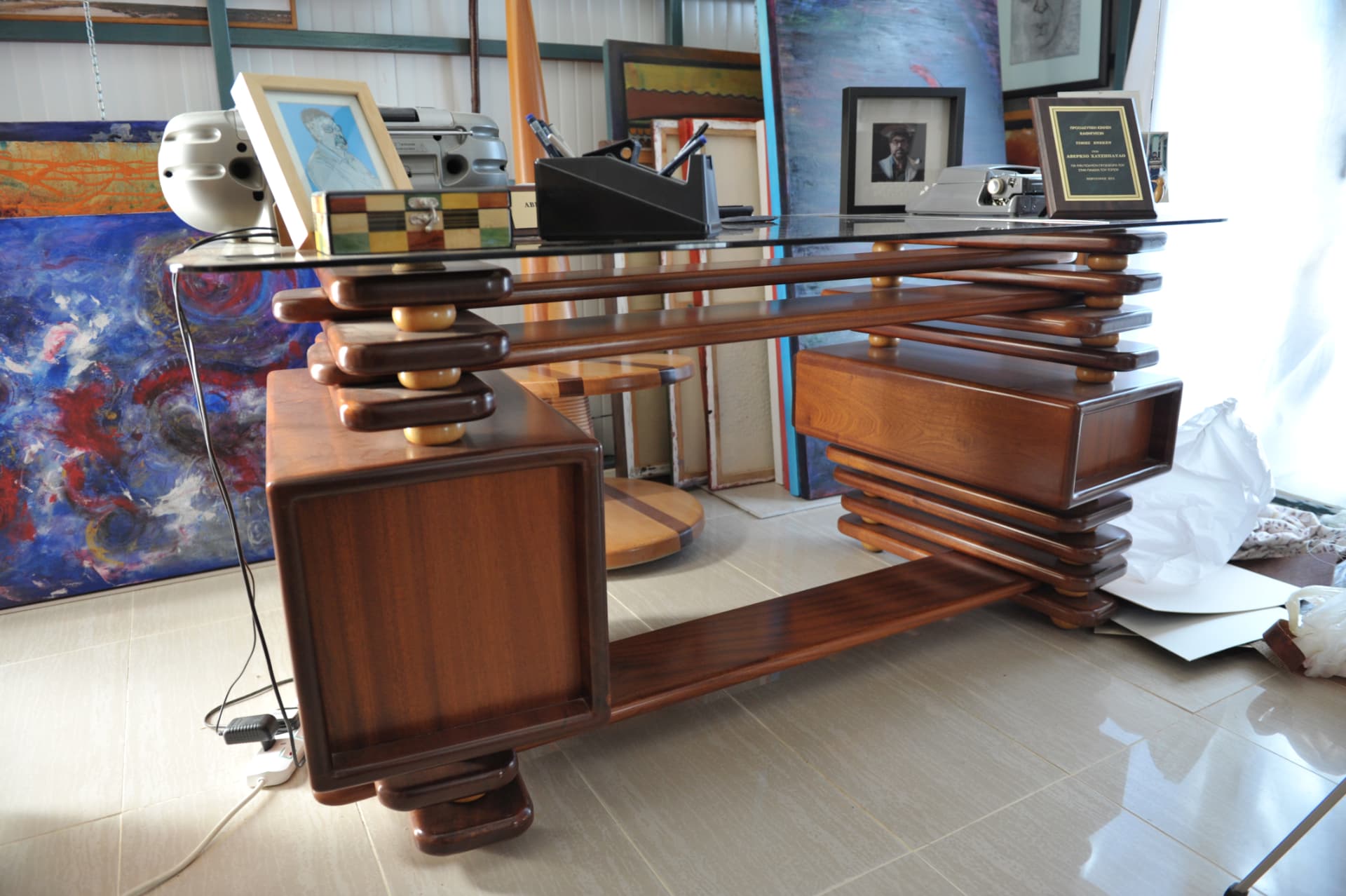 Wood desk with a glass top and tiered pedestals separated by small ball spacers, framed photos and a typewriter resting above