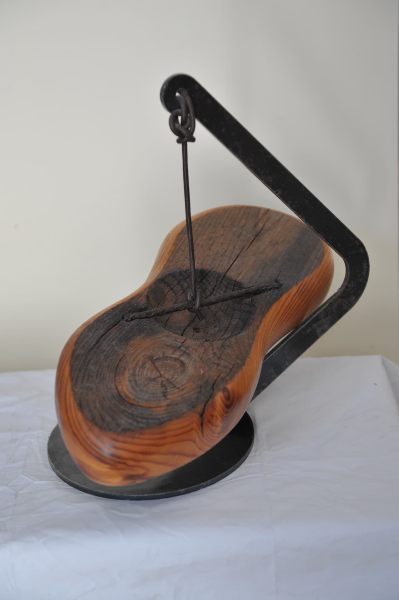 Oval wood piece with a carved dark centre suspended from a black stand