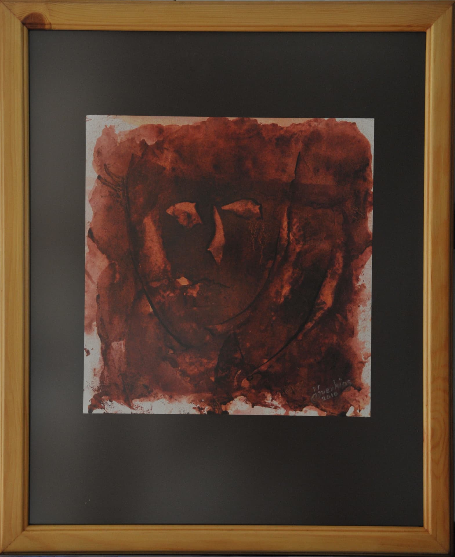Mask-like face formed from unpainted spaces within a deep reddish-brown wash, on paper mounted on a charcoal mat in a light wood frame